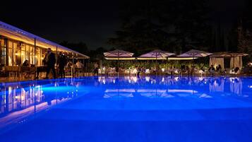 An outdoor pool area with tables and umbrellas, surrounded by trees.
