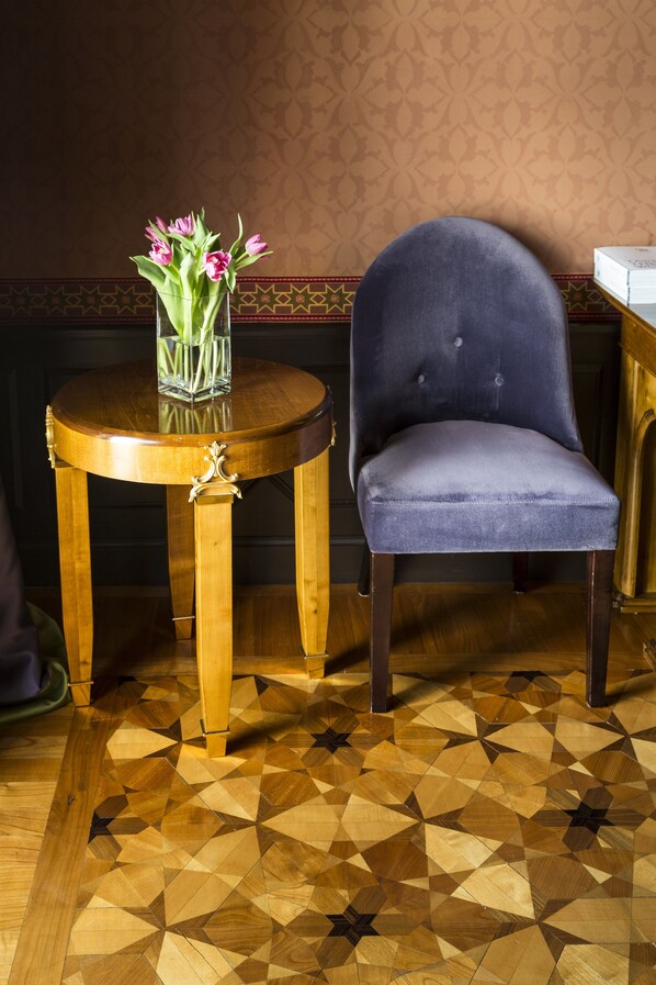 A round wooden table with a vase of pink flowers, a blue upholstered chair, and a patterned floor. - Villa Cora (Florence)