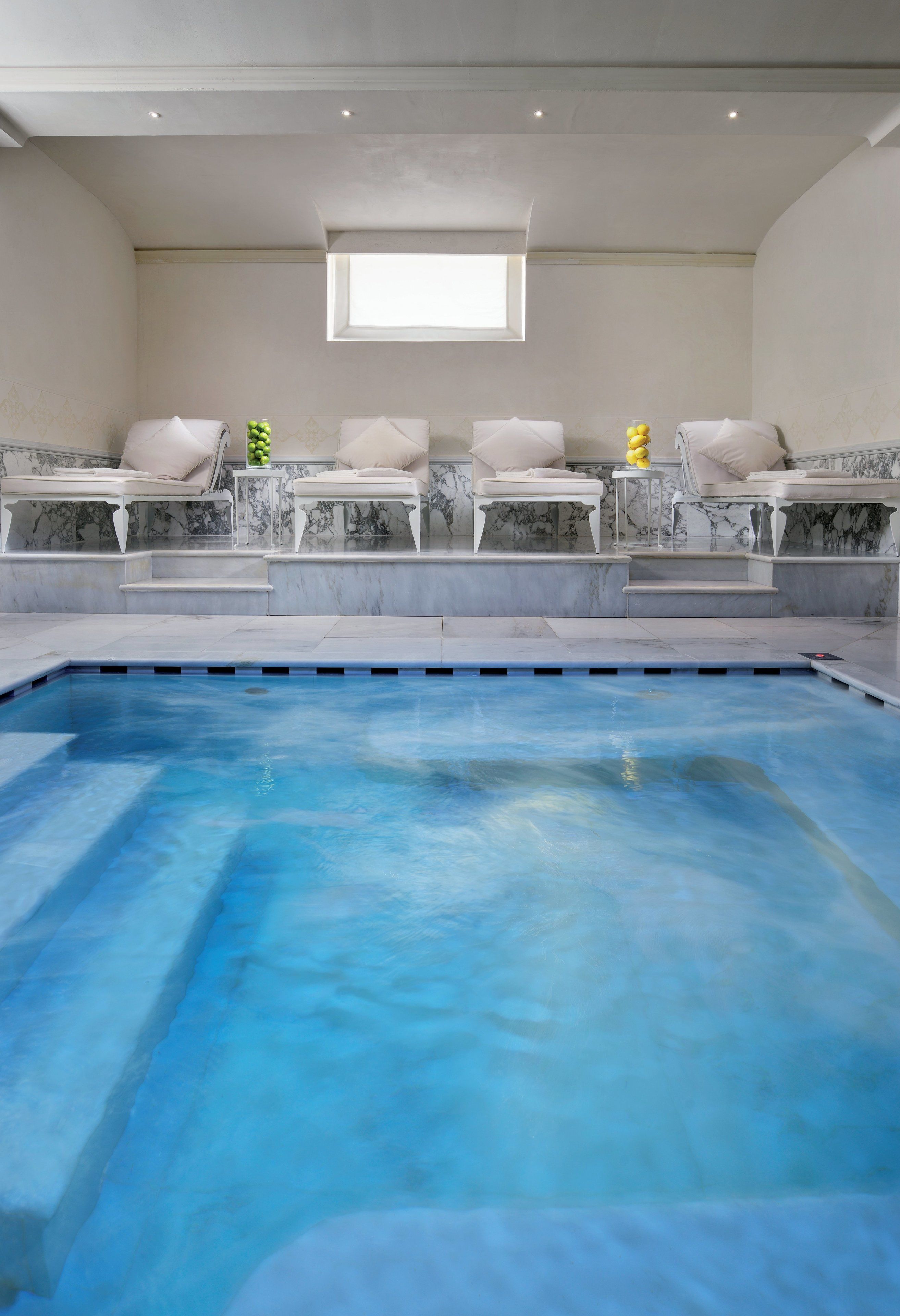 A swimming pool with a marble-lined deck and white cushioned seating areas.