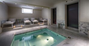 A spa area with a large rectangular hot tub, four lounge chairs, and a small window providing natural light.