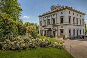 A large, classical building with a symmetrical facade, multiple windows, and a central entrance with a canopy. - Villa Cora (Florence)