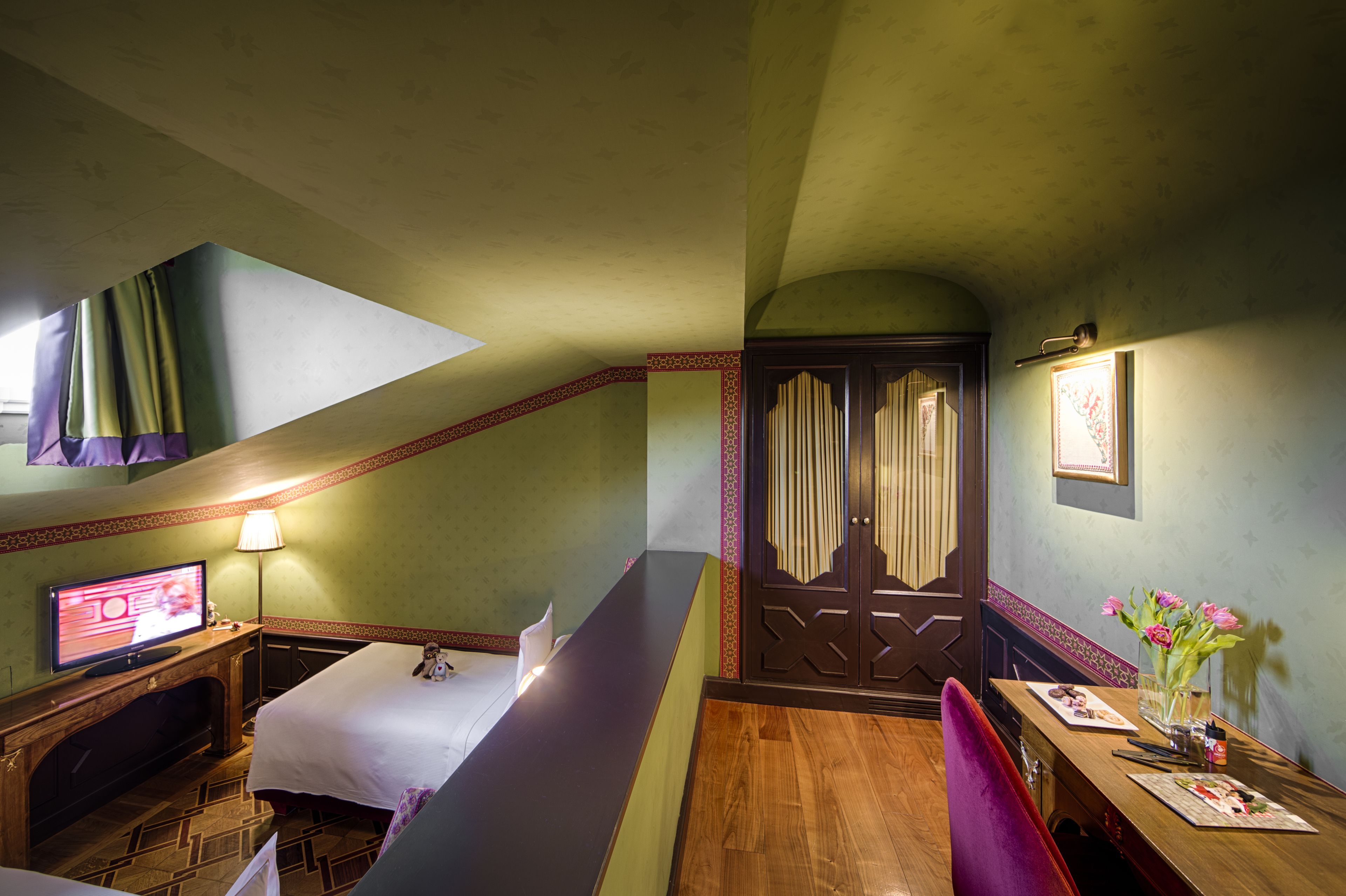 A hotel room with a bed, a desk with a lamp, a television, and a window with curtains.