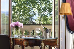 A table with a vase of flowers, a bottle of champagne, and glasses on a balcony with a view of trees.