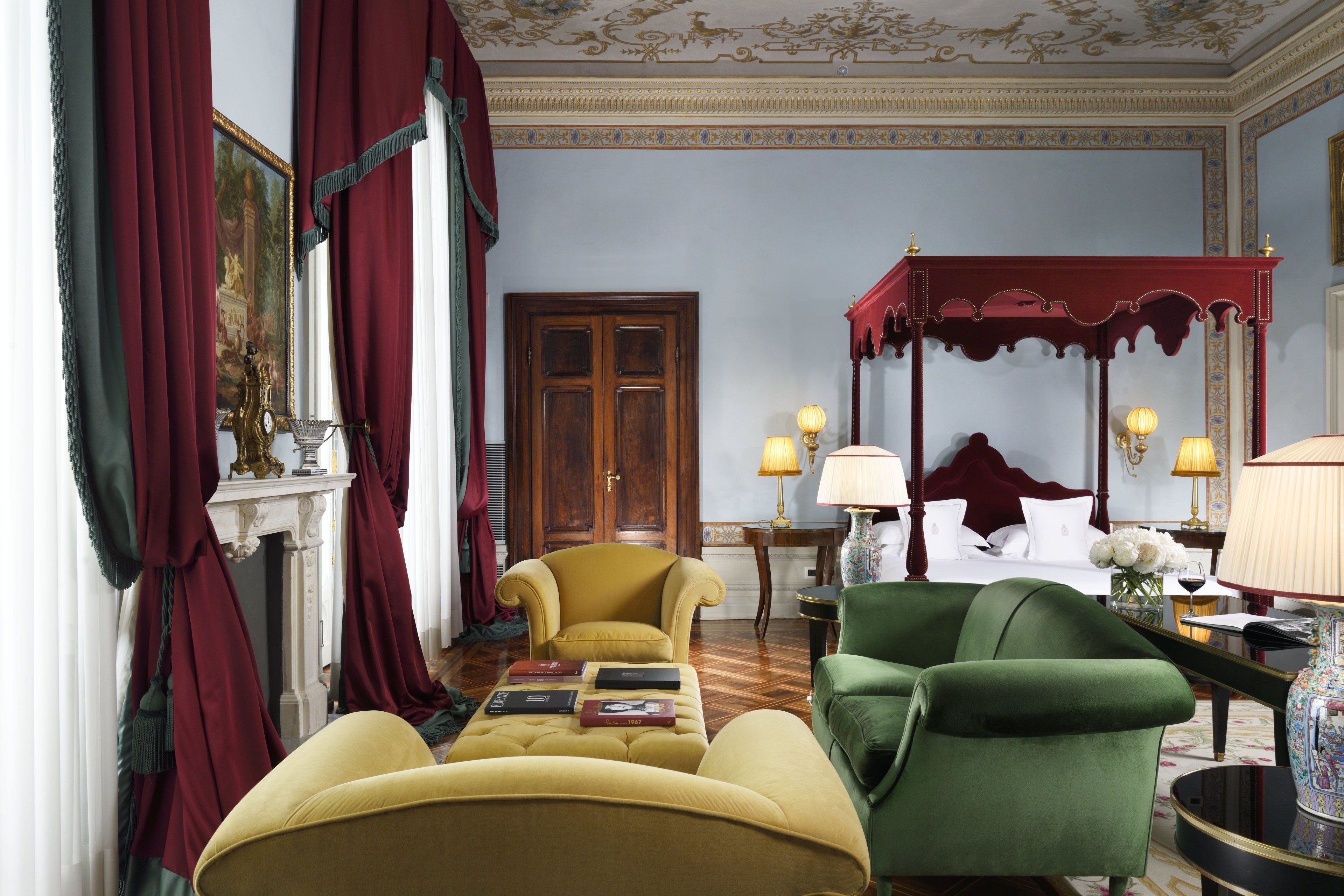A room with a four-poster bed, a green armchair, a yellow armchair, and a red canopy bed.