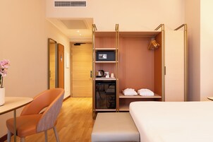 Une chambre d’hôtel équipée d’un lit, d’un bureau, d’une chaise, d’une armoire et d’une petite table avec une bouilloire et des tasses.