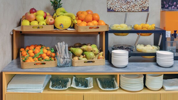 A buffet setup with various fruits and bowls of food, utensils, and plates arranged on a counter. - Hotel Raffaello (Milan)