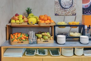 A buffet setup with various fruits and bowls of food, utensils, and plates arranged on a counter. - Hotel Raffaello (Milan)