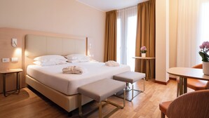 A hotel room with a large bed, a bedside table, a small table with a plant, and a chair. - Hotel Raffaello (Milan)