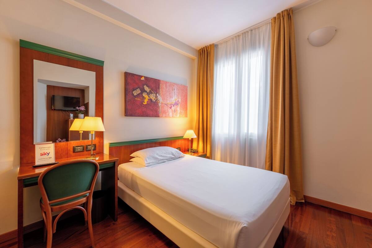 Una camera d'albergo con un letto, una scrivania con una sedia, una televisione e un quadro appeso al muro.