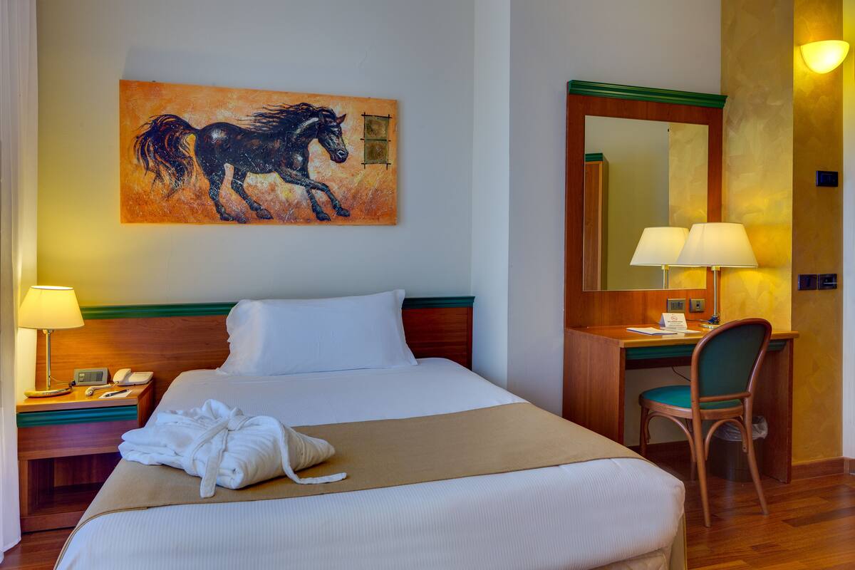 Una camera d'albergo con un letto, una scrivania, una sedia, un quadro e uno specchio.