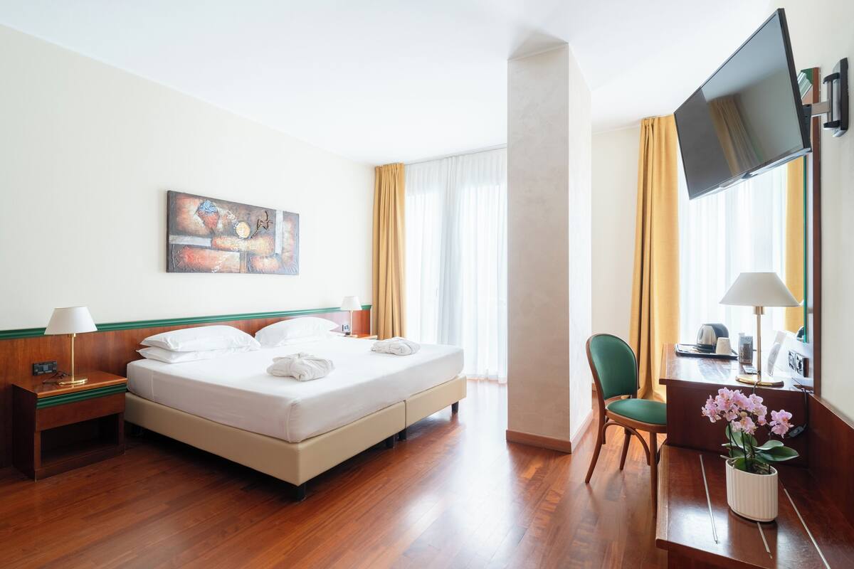 Una camera d'albergo con un letto, una scrivania, una sedia, una TV e un quadro appeso al muro.