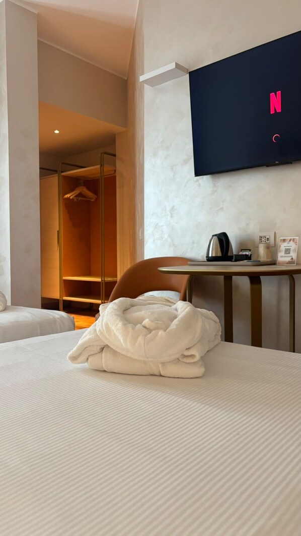 A hotel room with a bed, a TV mounted on the wall, a table with a kettle, and a wardrobe.