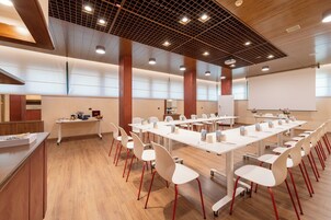 Μια αίθουσα συνεδριάσεων με λευκά τραπέζια και καρέκλες, ξύλινο δάπεδο και ένα μοντέρνο σχέδιο στην οροφή.