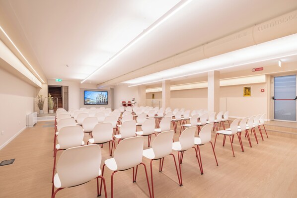 A conference room with rows of white chairs and a large screen at the front. - Hotel Raffaello (Milan)