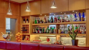 A bar area with wooden shelves stocked with various liquor bottles, a glass display case, and a potted plant. - Hotel Raffaello (Milan)
