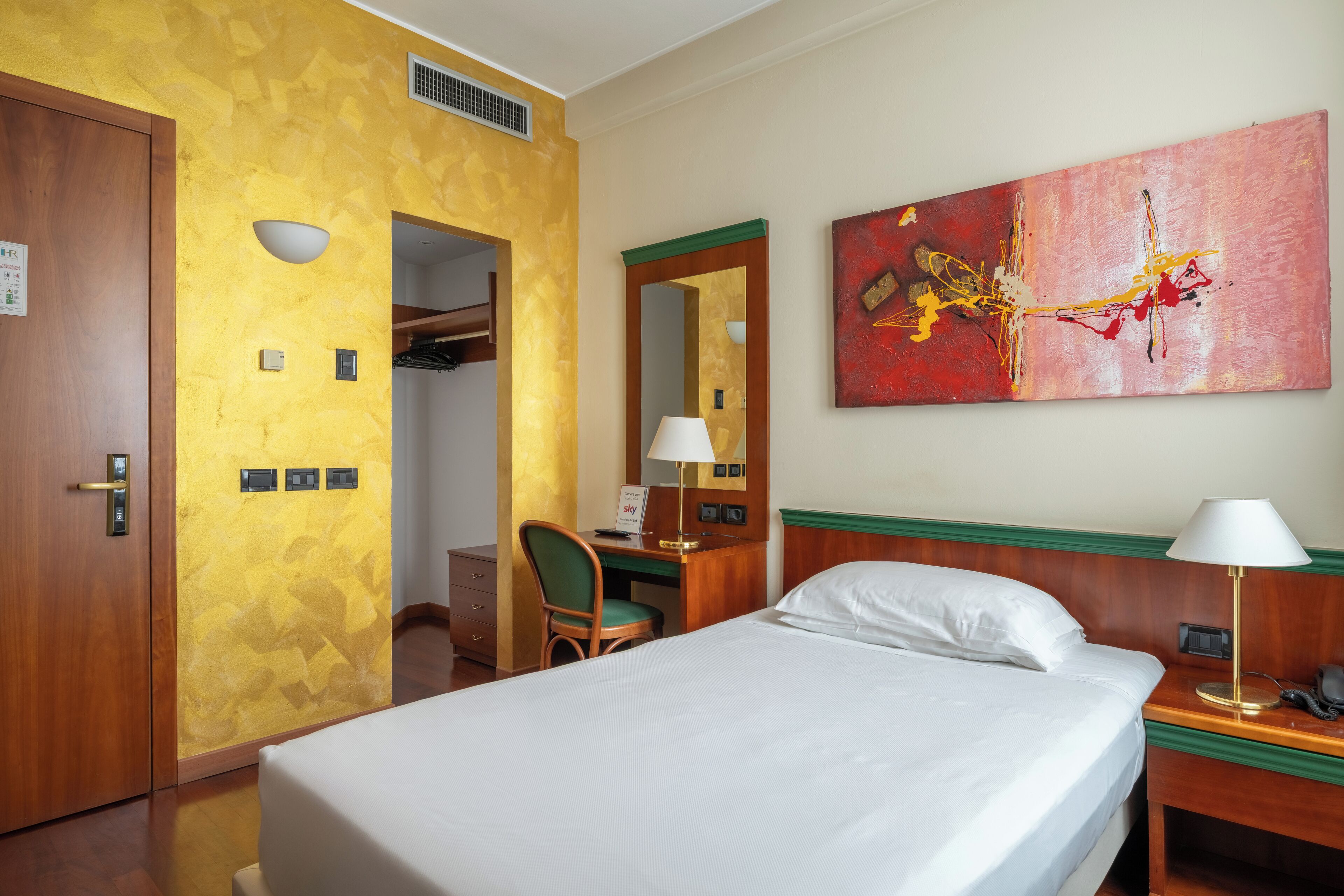 Habitación de hotel con cama, escritorio, silla, lámpara de escritorio, teléfono y un cuadro en la pared.