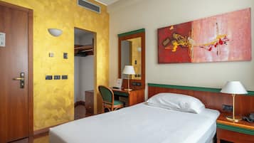 Habitación de hotel con cama, escritorio, silla, lámpara de escritorio, teléfono y un cuadro en la pared.