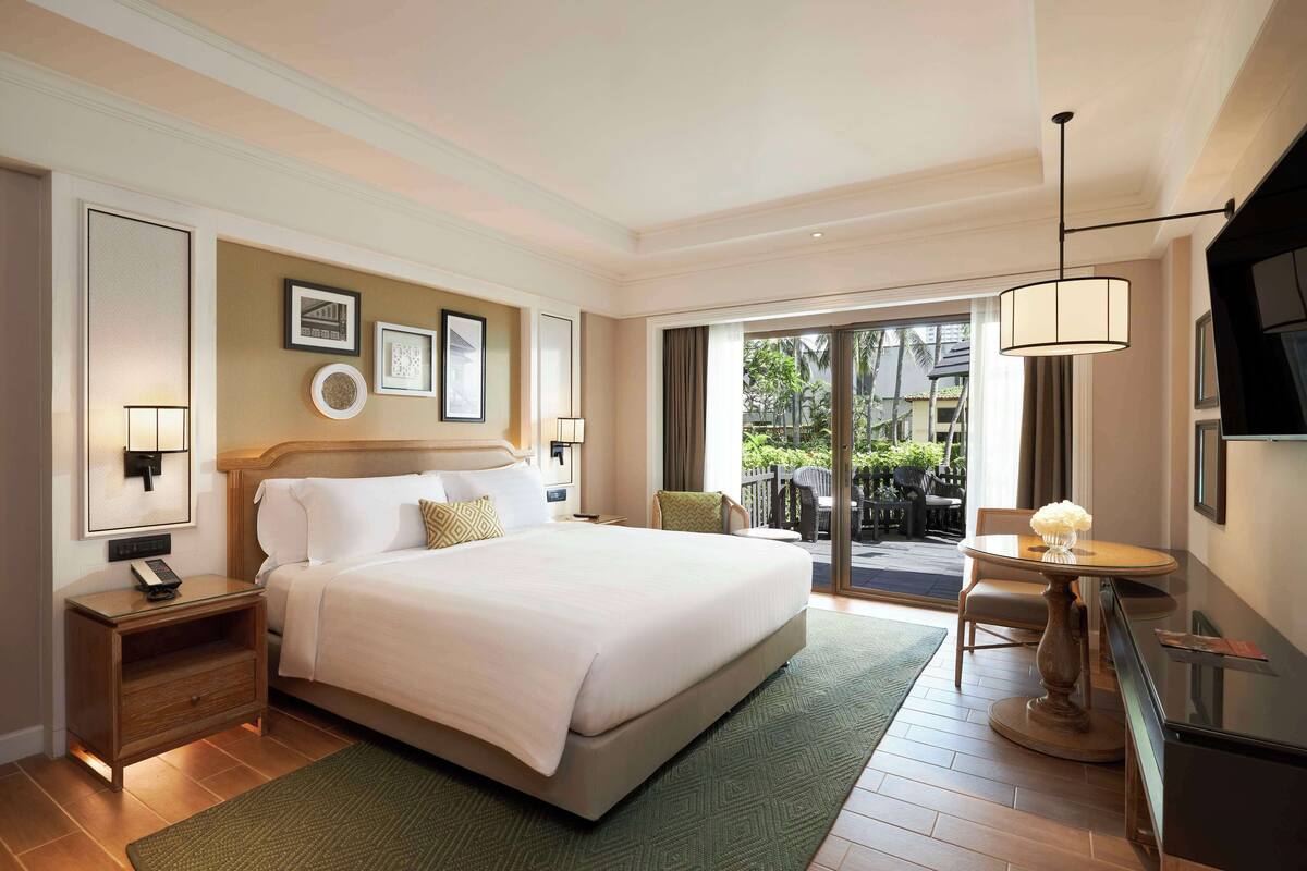 Habitación de hotel con una cama grande, un escritorio con lámpara, una silla y vistas al exterior.