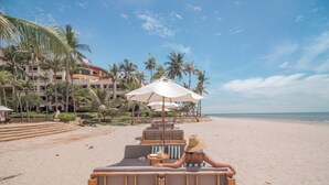 Un salon de plage doté de sièges en bois, bordé de palmiers et offrant une vue sur l’océan.