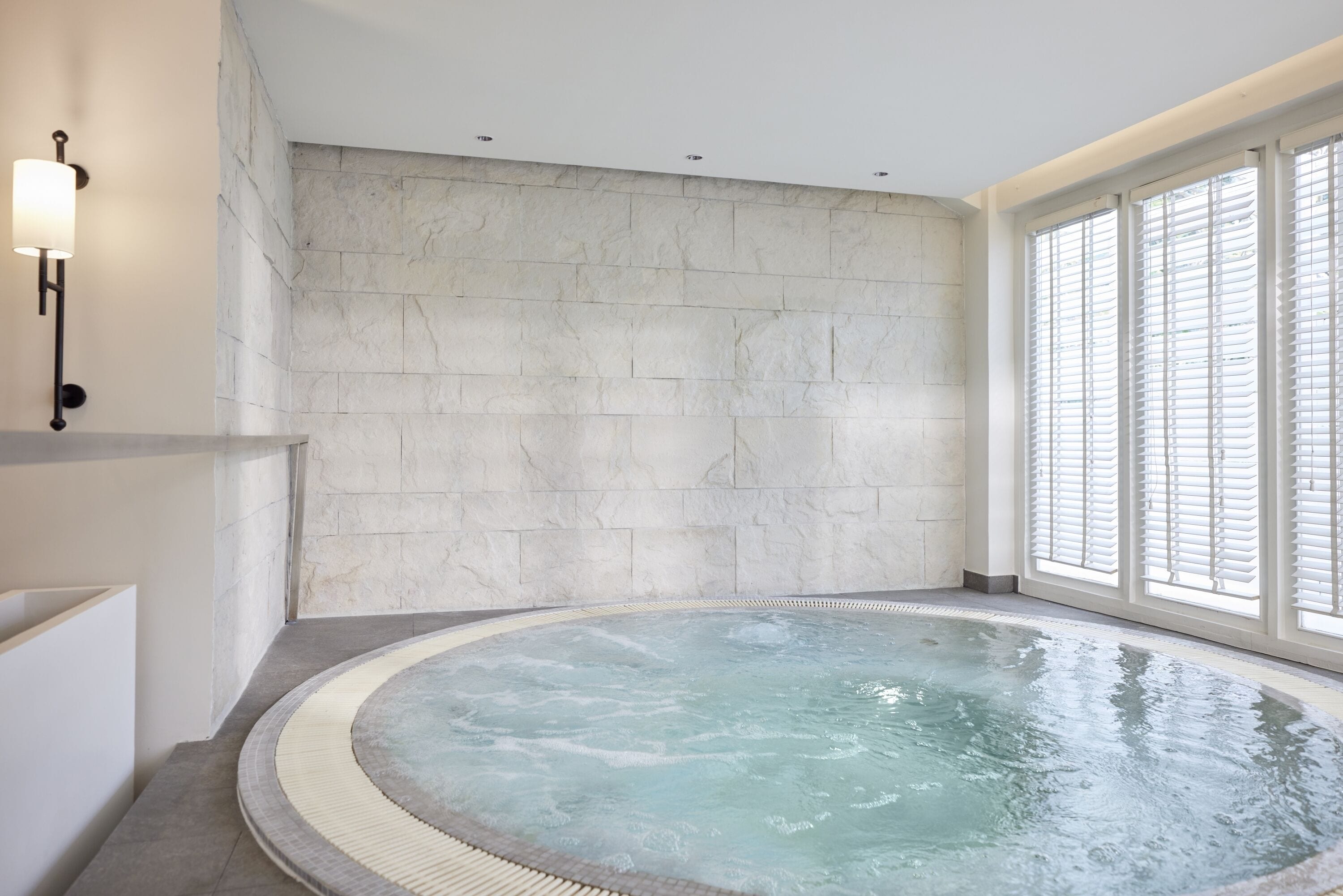 Une salle de spa dotée d’un bain à remous, de murs en pierre et de grandes fenêtres.