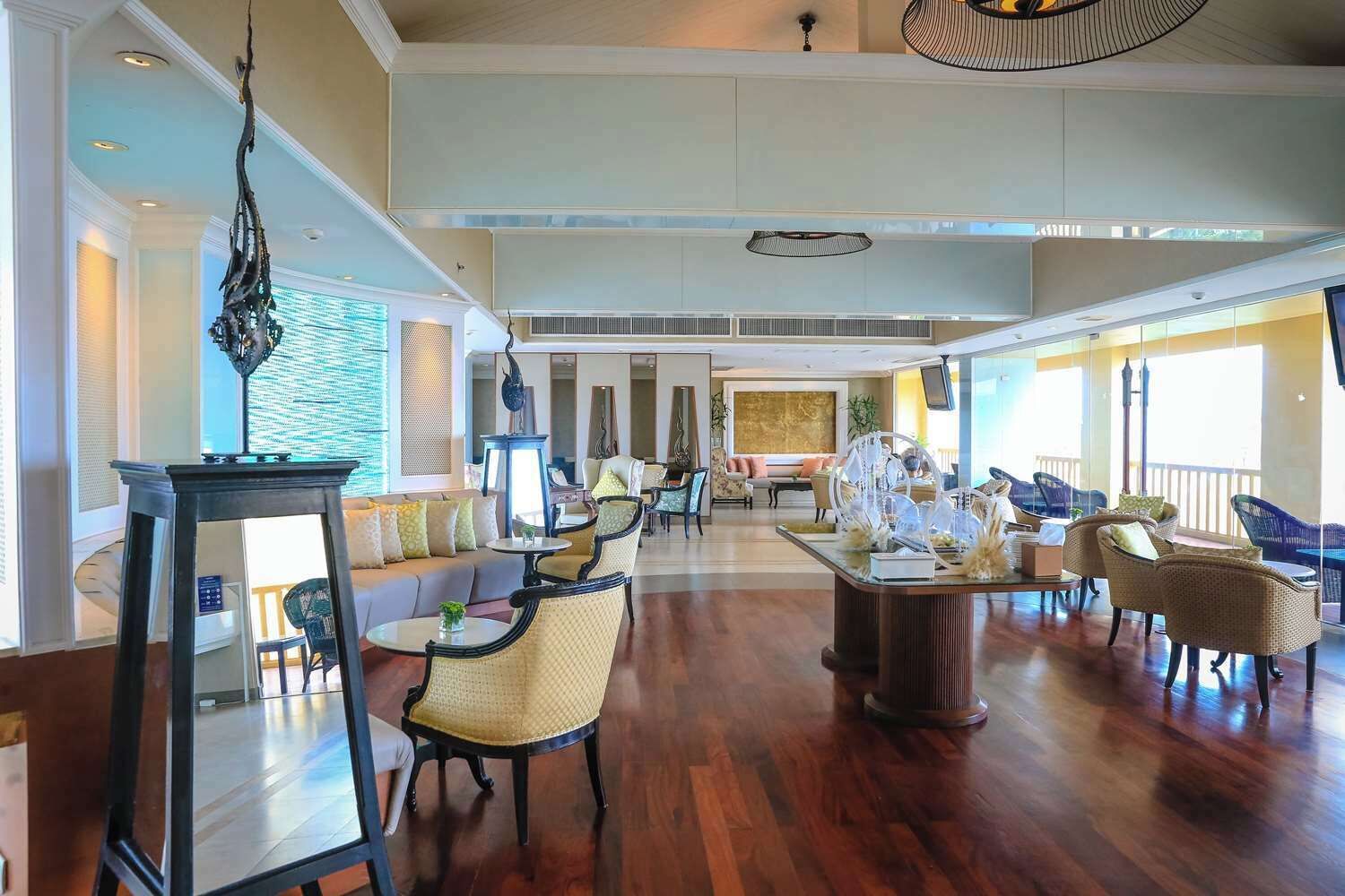 A spacious lobby with a high ceiling, a central seating area with multiple chairs and sofas, and a large table with decorative items.