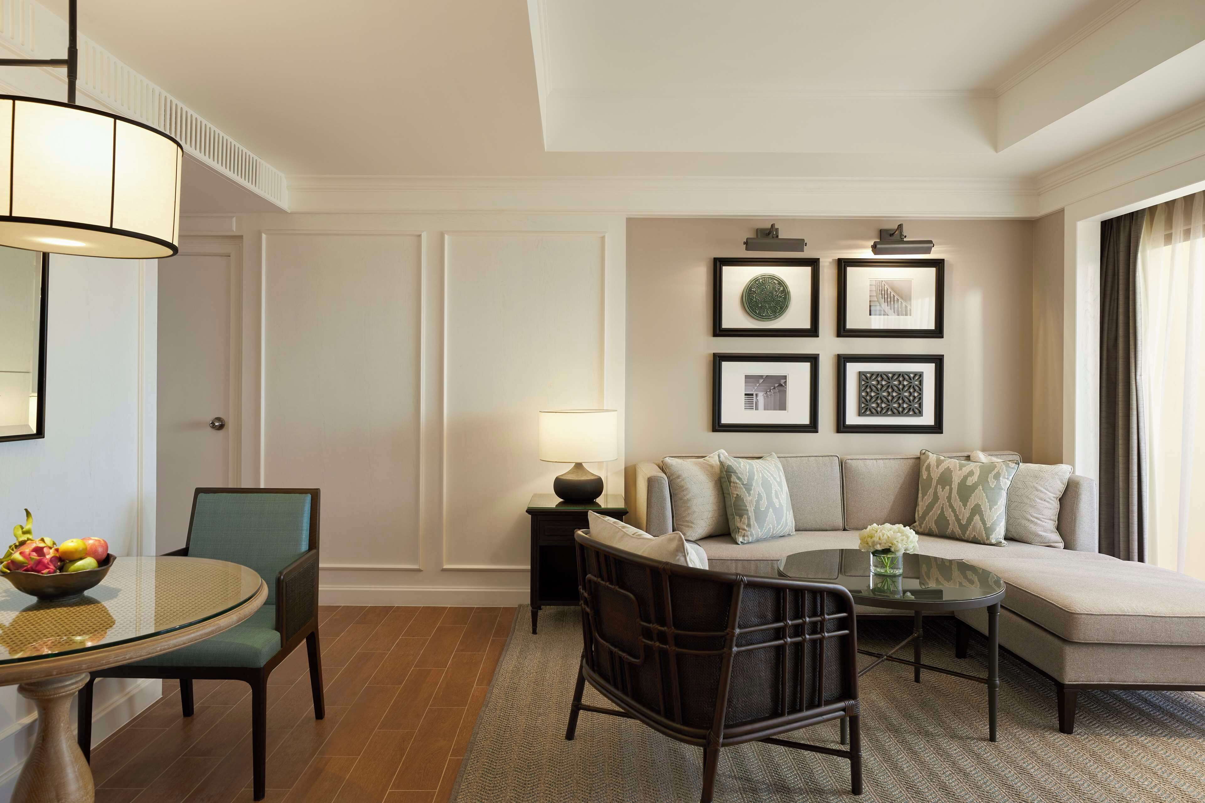 A modern living room with a round glass table, a sofa, and a chair. There are framed pictures on the wall and a lamp on a side table.