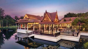 A traditional-style building with a reflective water body in front, featuring a bridge and a gazebo. - Dusit Thani Hua Hin (Cha-am)