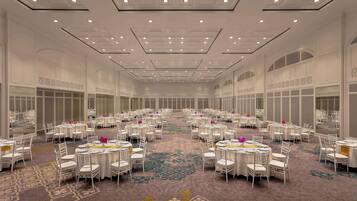 Un amplio salón de banquetes con mesas y sillas redondas, una alfombra estampada y un techo alto con iluminación empotrada.