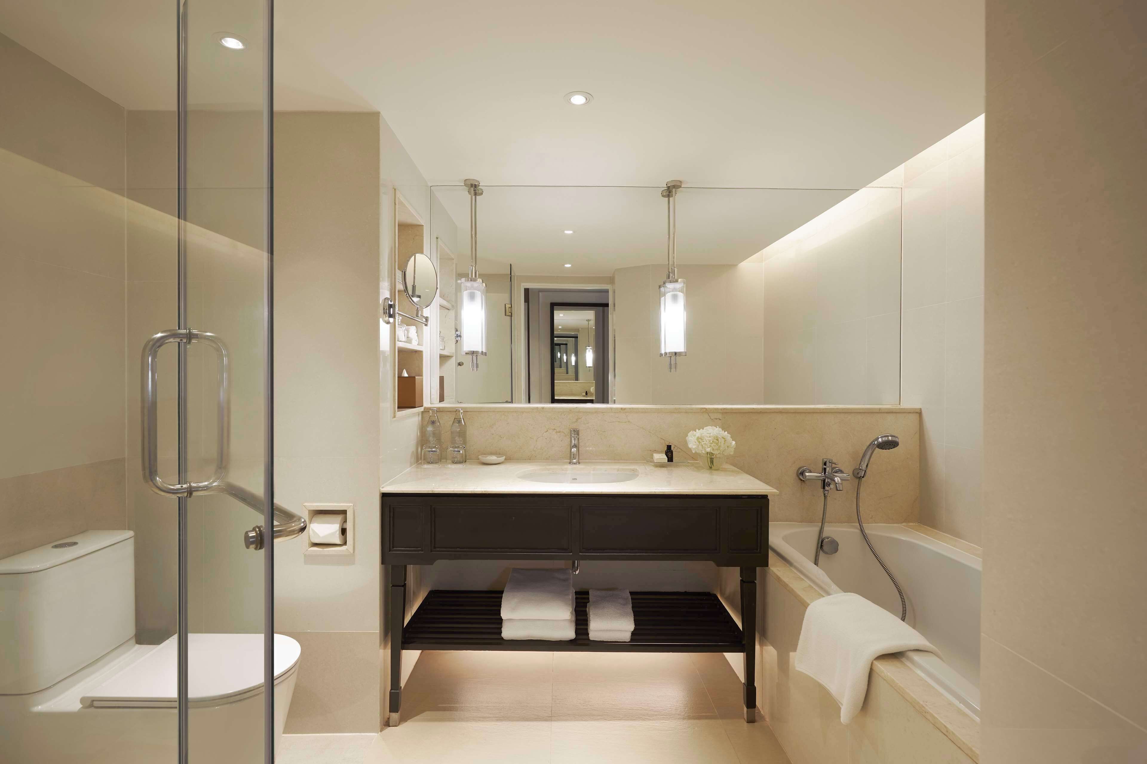 Un baño moderno con ducha de vidrio, un espejo grande, un lavabo con toallero y una bañera.