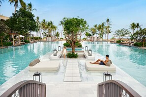Un espace aménagé au bord de la piscine, avec des chaises longues, un arbre et un chemin menant à la piscine.