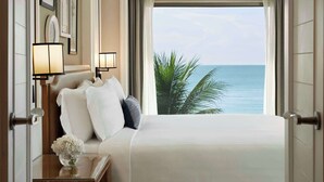 A hotel room with a large bed, a nightstand, a lamp, and a view of the ocean. - Dusit Thani Hua Hin (Cha-am)