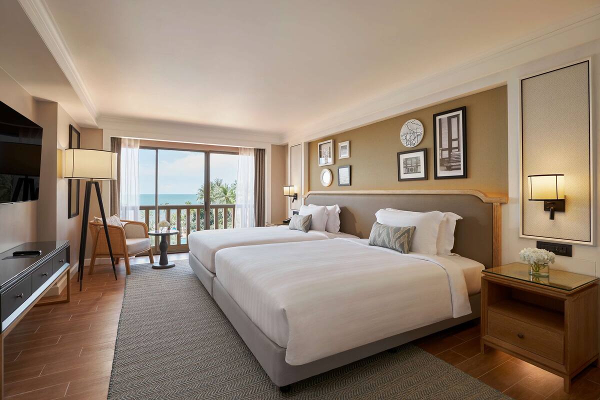 Habitación de hotel con dos camas, un escritorio, una silla, un televisor y un balcón con vista al mar.