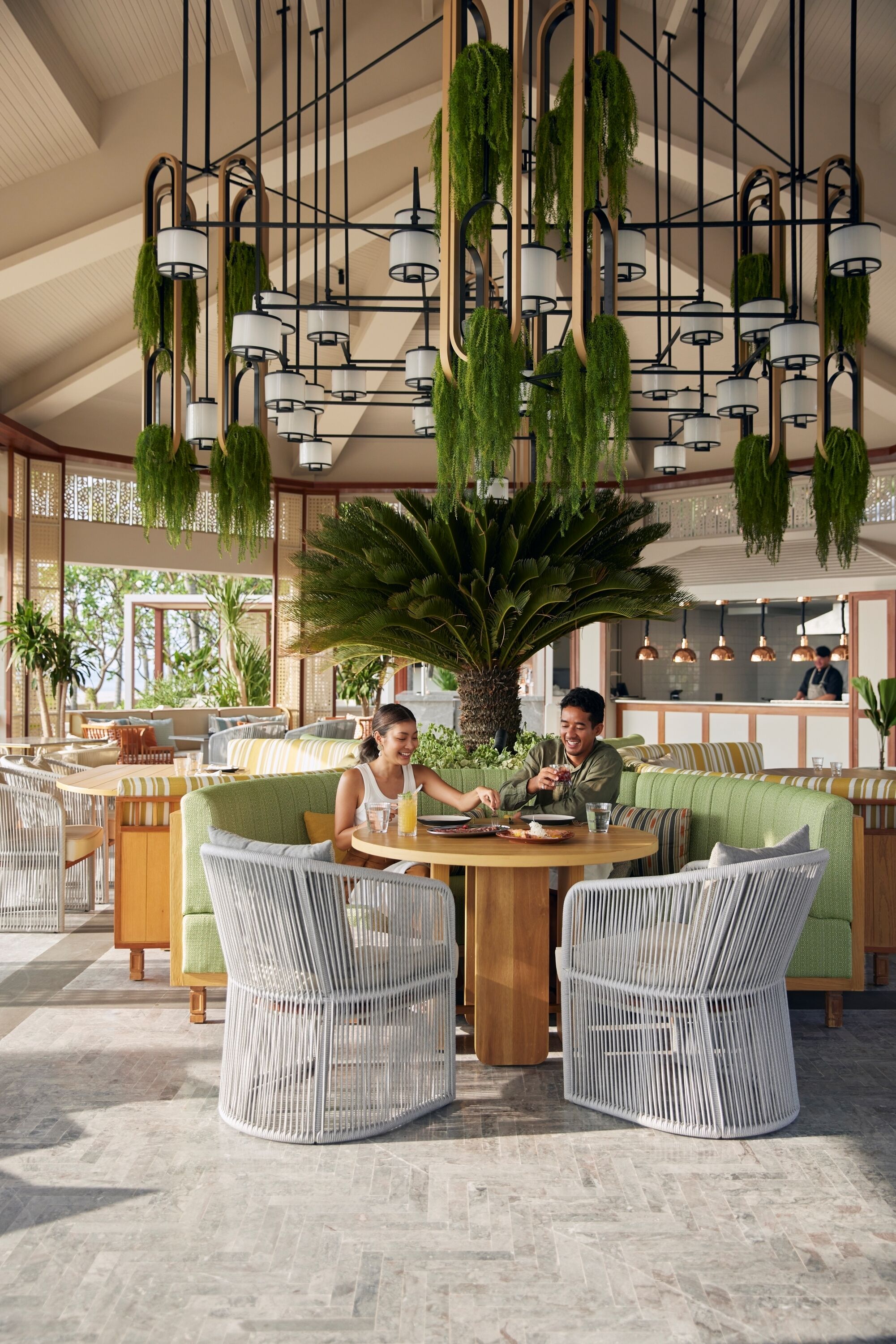Un restaurant doté de meubles en osier, de plantes suspendues et d’une grande plante centrale.