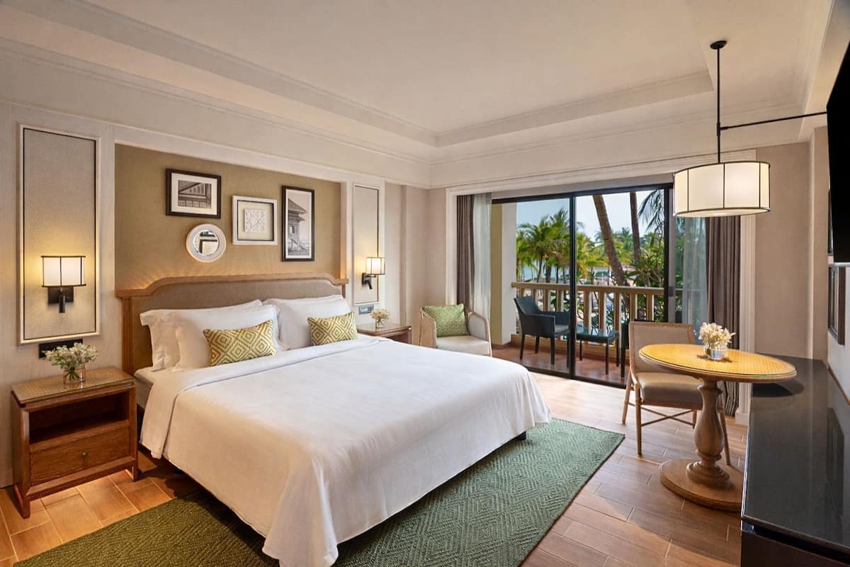 Una habitación de hotel con una cama grande, un balcón con mesa y sillas, y un televisor.