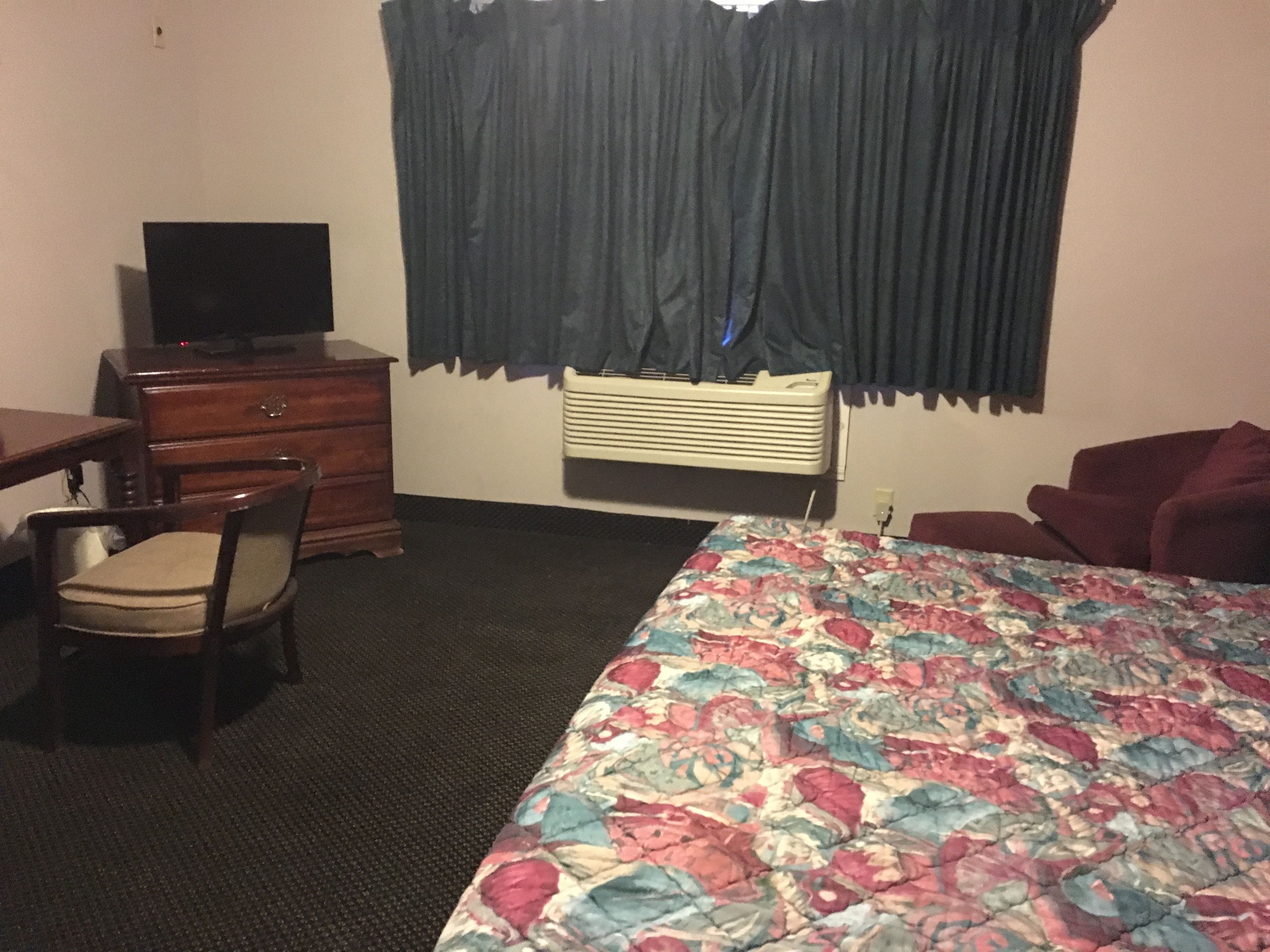 A hotel room with a bed, a desk, a chair, a television, and a window with curtains.