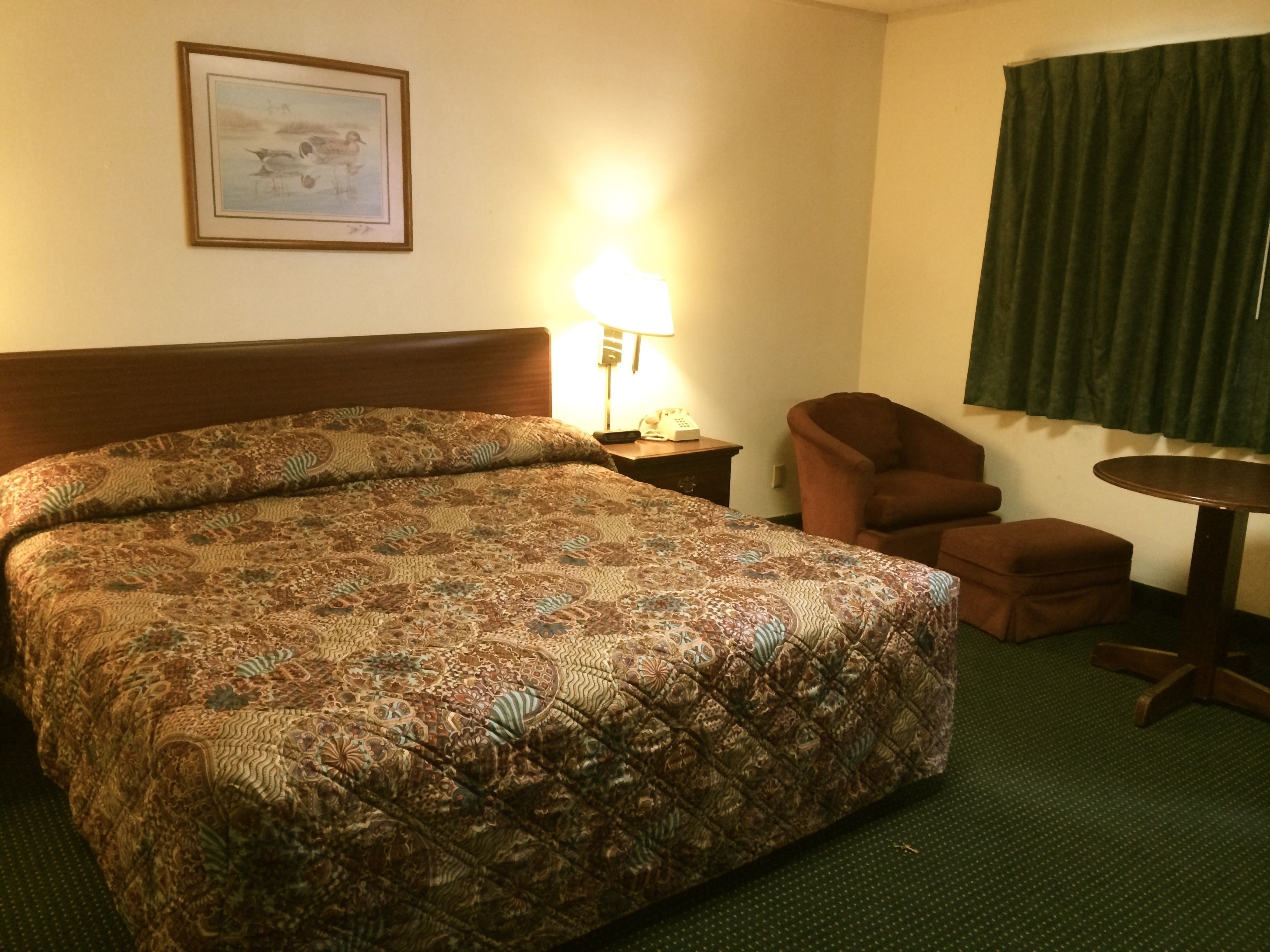 Una camera d'albergo con un letto grande, una poltrona, un tavolino e una lampada.