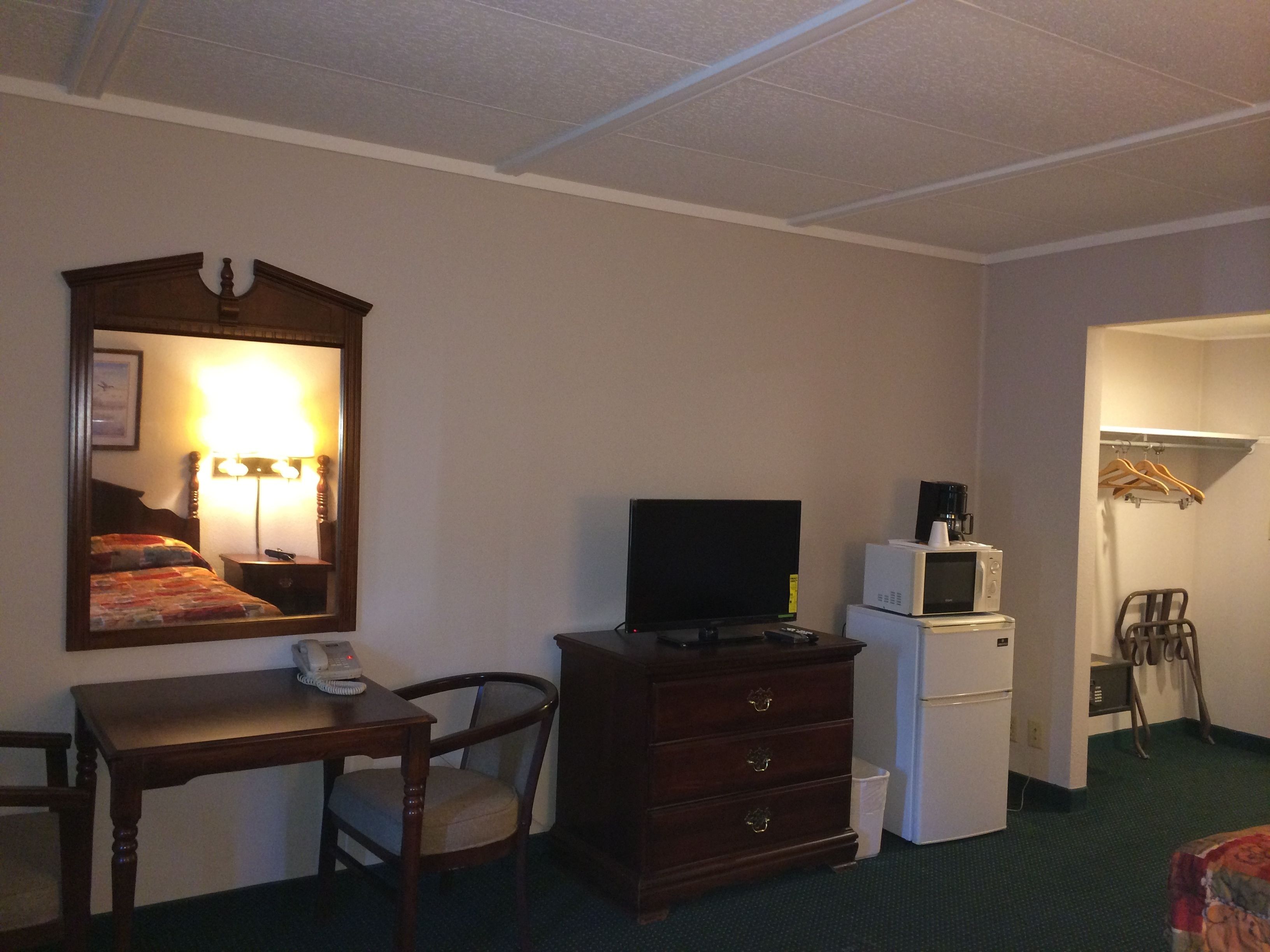 Habitación de hotel con cama, cómoda, escritorio con teléfono, televisor, microondas y armario con perchas.