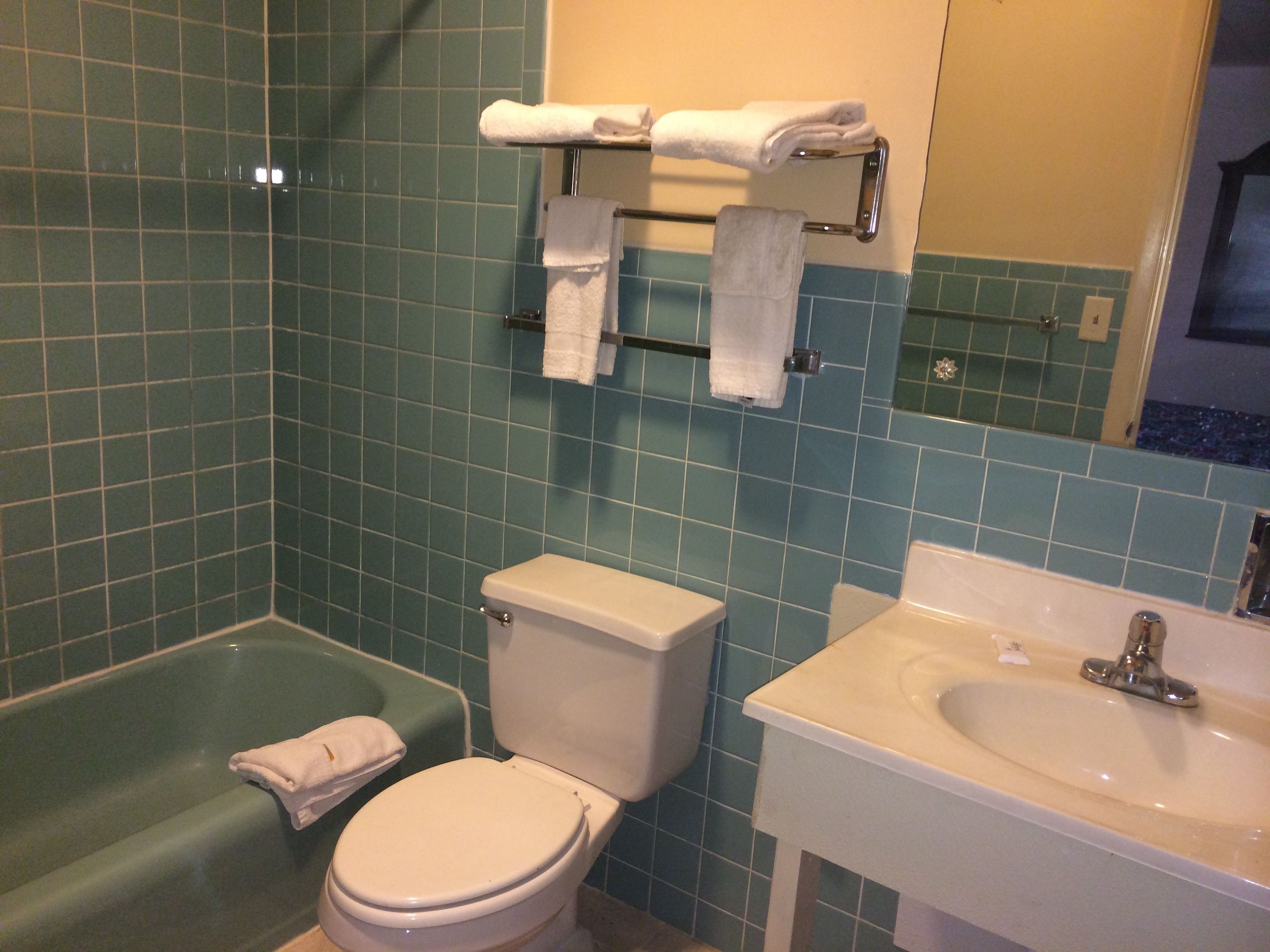 Une salle de bain avec un mur recouvert de carreaux verts, des toilettes blanches, une baignoire verte et un lavabo avec un miroir au-dessus.