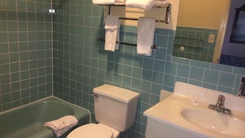 Une salle de bain avec un mur recouvert de carreaux verts, des toilettes blanches, une baignoire verte et un lavabo avec un miroir au-dessus.