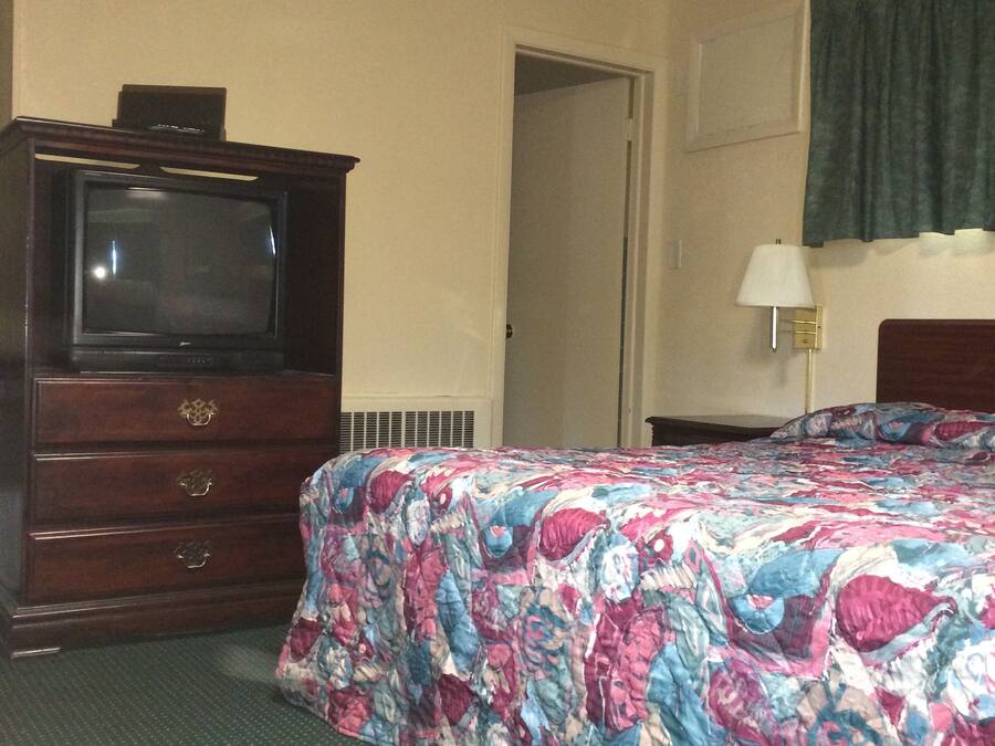 Una habitación de hotel con cama, cómoda, televisor, puerta y lámpara.
