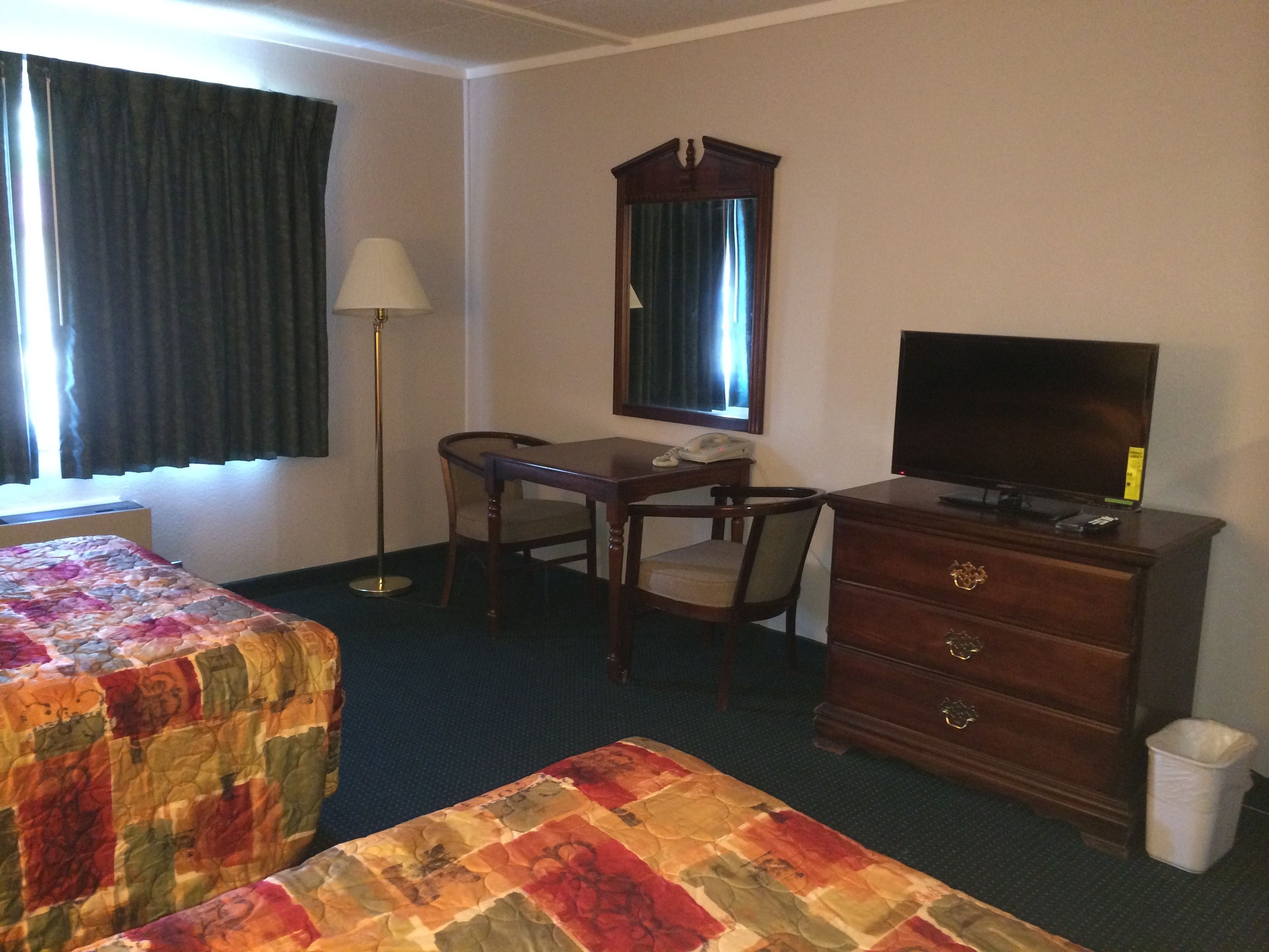 Habitación de hotel con dos camas, un escritorio con silla, cómoda, televisor y ventana con cortinas.
