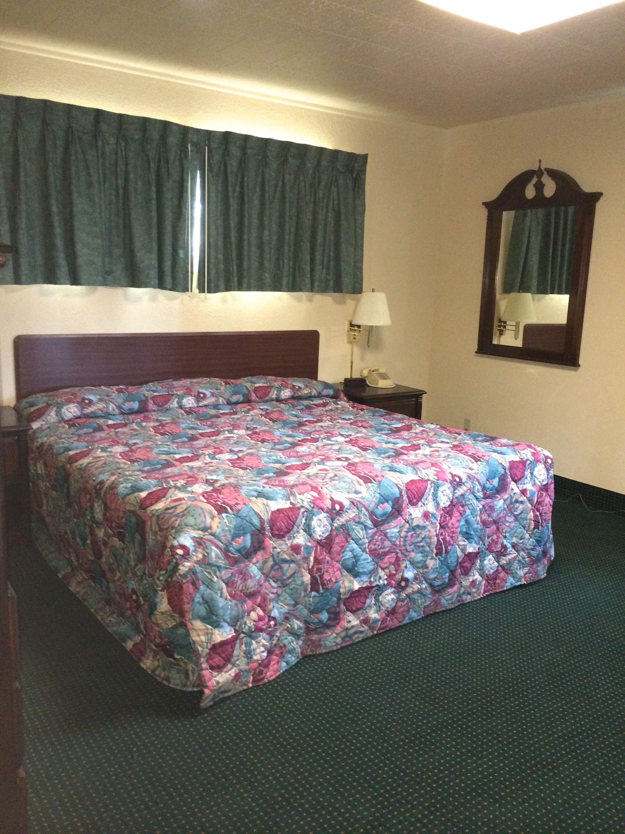 A hotel room with a large bed, a nightstand, a lamp, a mirror, and a window with curtains.