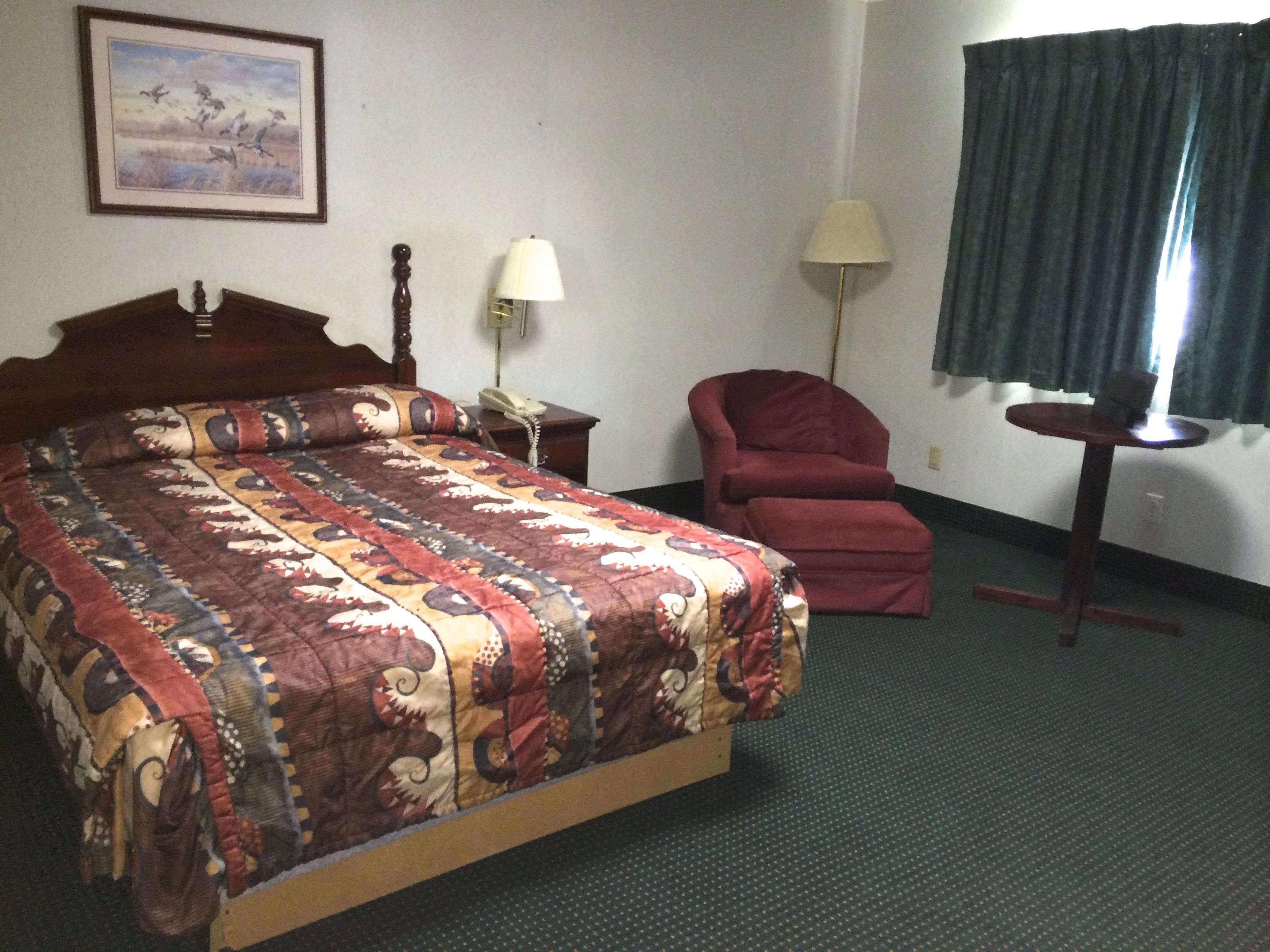 Ein Hotelzimmer mit einem großen Bett, einem Sessel, einem Schreibtisch, einer Lampe und einem Gemälde an der Wand.