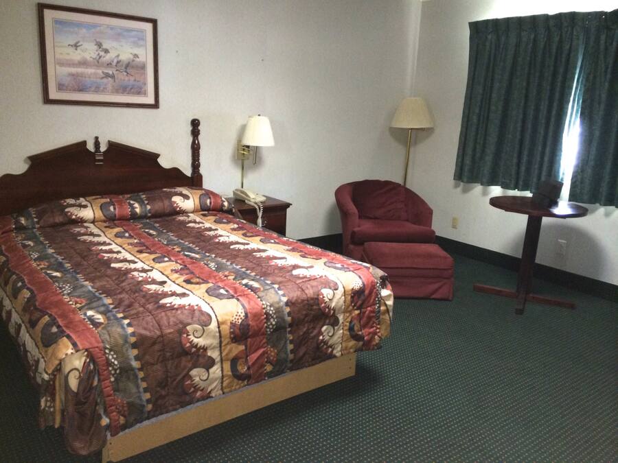 Ein Hotelzimmer mit einem großen Bett, einem Sessel, einem Schreibtisch, einer Lampe und einem Gemälde an der Wand.