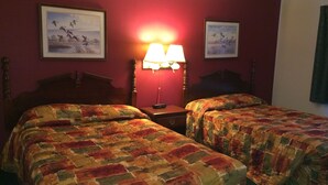 A hotel room with two beds, a nightstand, a lamp, and two framed pictures on the wall. - Rapids Inn and Suites (Wisconsin Rapids)