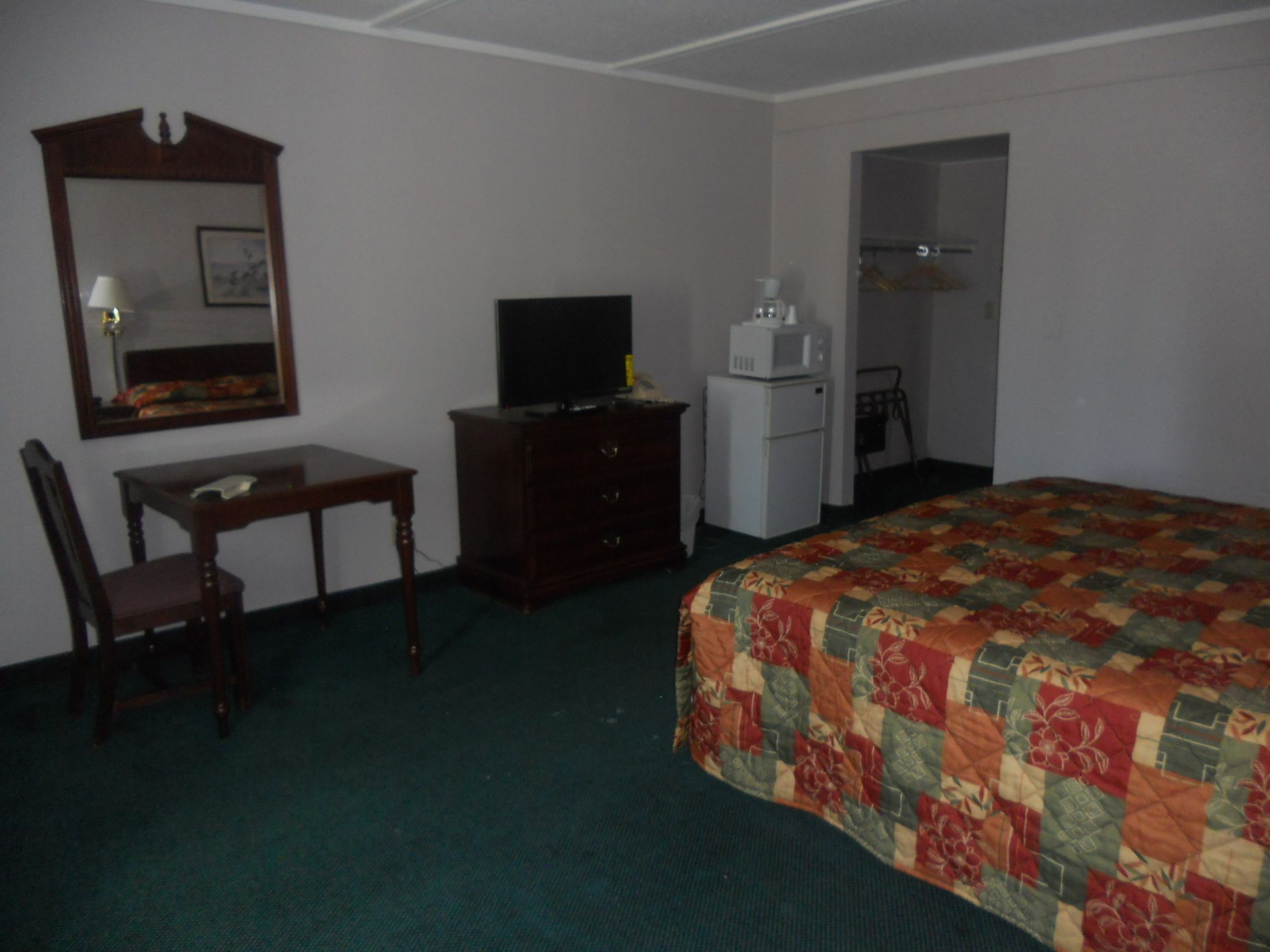 A hotel room with a bed, a desk, a television, a refrigerator, and a mirror.