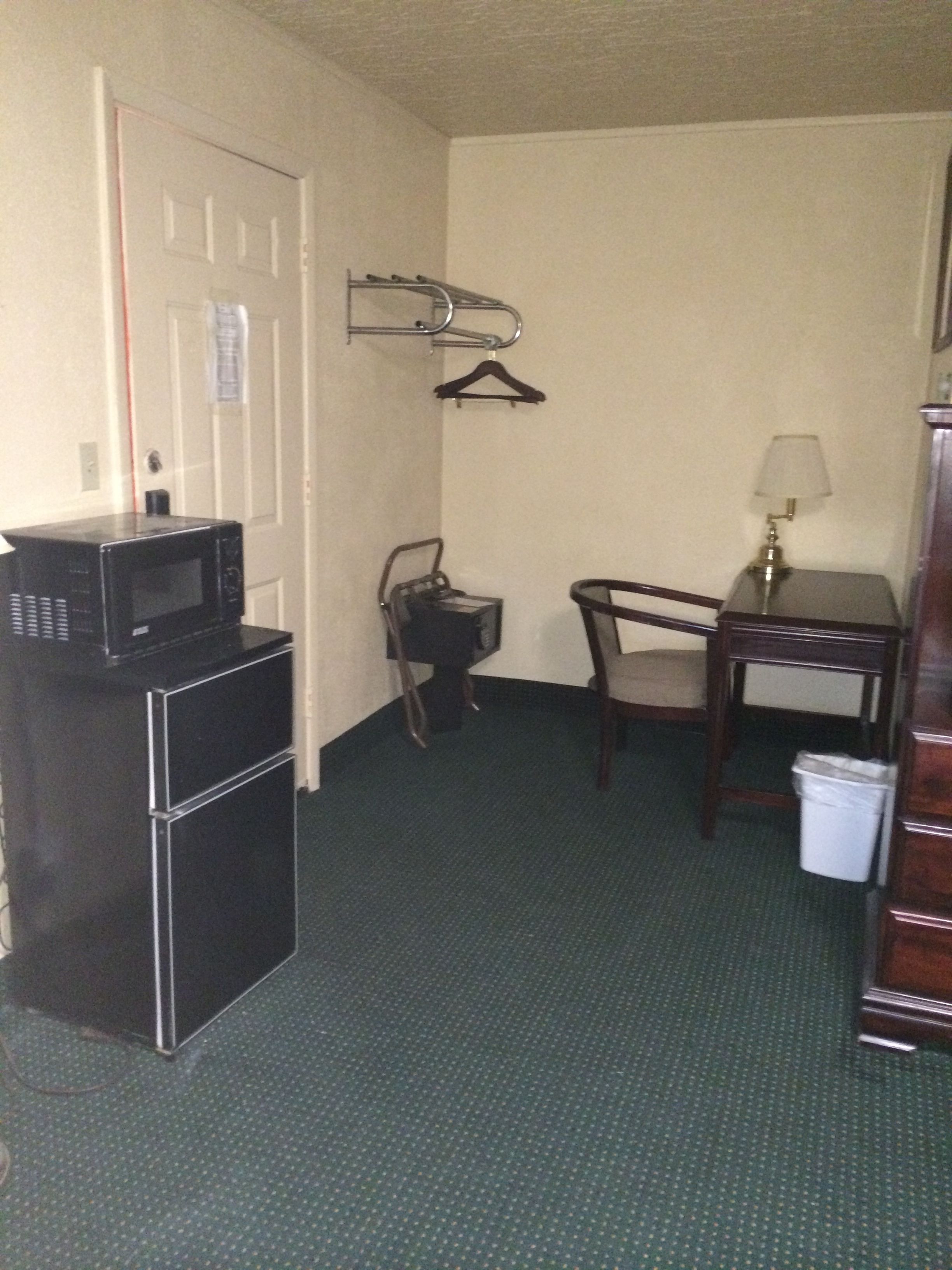 Une chambre d’hôtel compacte comprenant un coin cuisine, une chaise, une petite table avec une lampe et un porte-manteau.