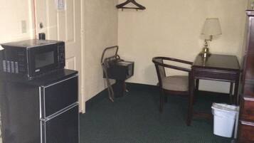 Une chambre d’hôtel compacte comprenant un coin cuisine, une chaise, une petite table avec une lampe et un porte-manteau.