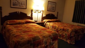A hotel room with two single beds, a nightstand, a lamp, and two framed pictures on the wall.