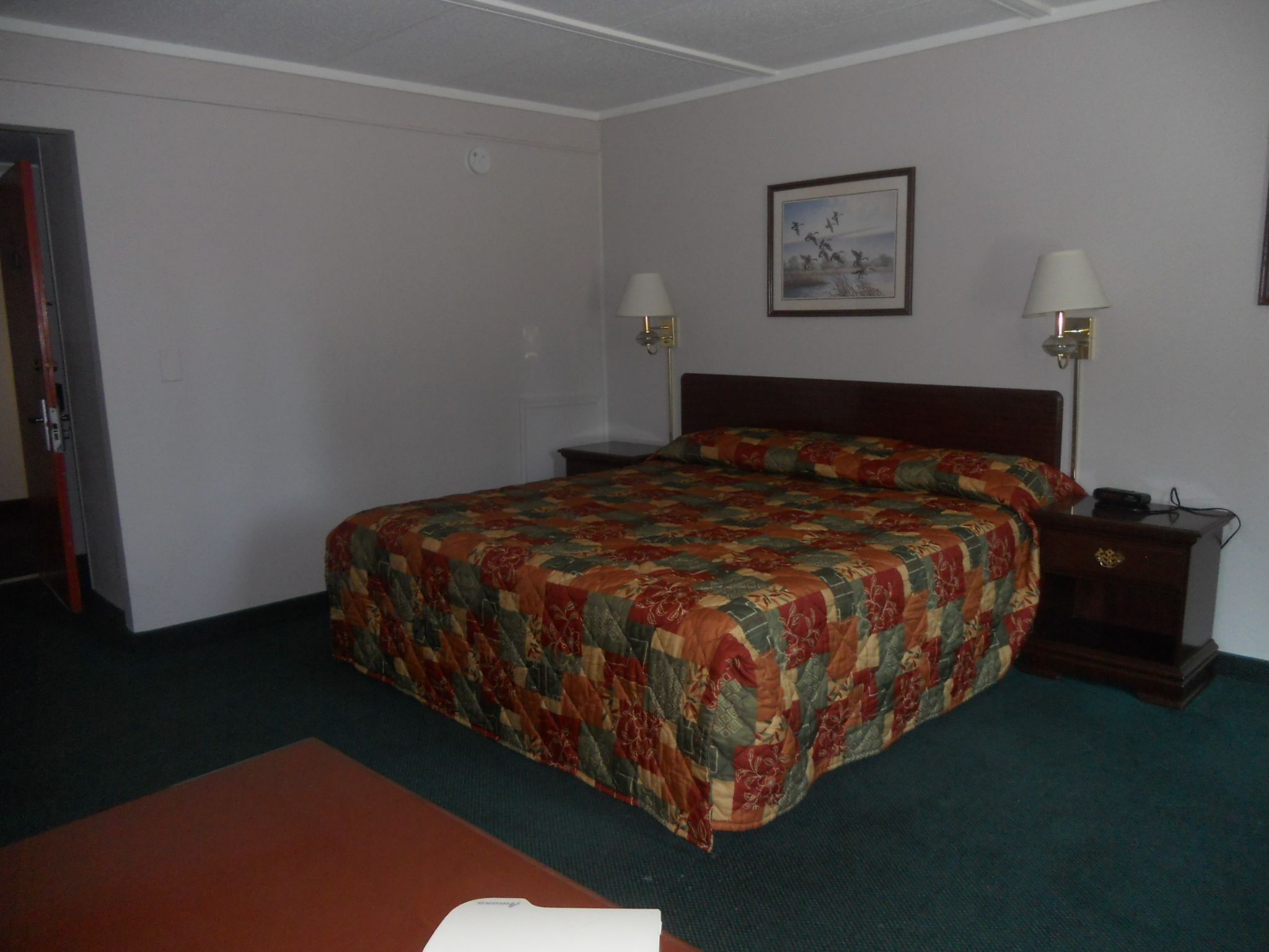 A hotel room with a large bed, two bedside tables with lamps, a painting on the wall, and a door to the left.